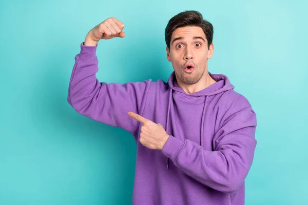 Bild av stark imponerad ung kille klädd violett tröja pekar finger armar muskler stora ögon isolerad turkos färg bakgrund — Stockfoto
