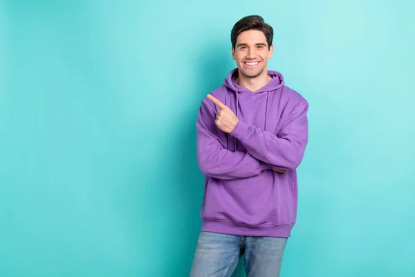 Foto di funky attraente giovane uomo indossare felpa viola con cappuccio sorridente indicando dito vuoto spazio isolato colore verde acqua sfondo — Foto Stock