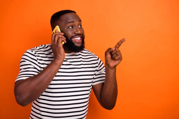 Fotografie mladého afrického chlapa mluvit smartphone indikovat prst prázdný prostor vybrat navrhnout promo izolované přes oranžové barvy pozadí — Stock fotografie