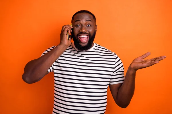 Фото молодого веселого африканца, говорящего на смартфоне, хорошая новость изолирована на фоне оранжевого цвета — стоковое фото