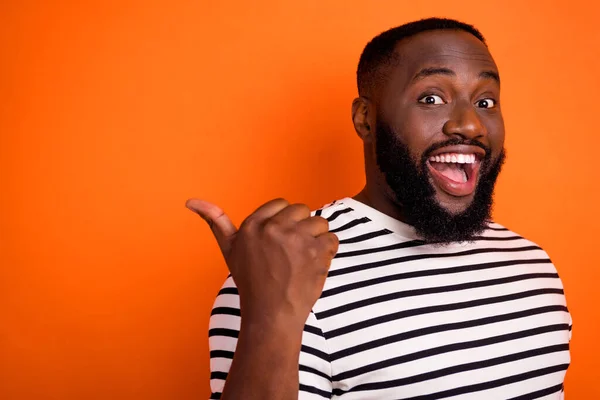 Foto del lado del perfil de un joven africano excitado que señala con el dedo la promoción de anuncios de espacio vacío aislado sobre fondo de color naranja — Foto de Stock