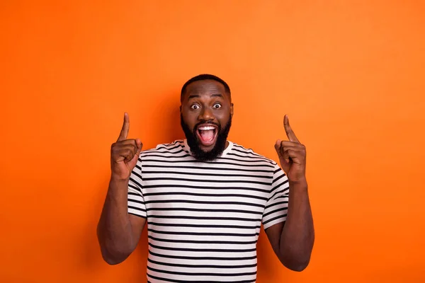 Фото молодого взволнованного африканца показывает пальцы пустые пространство промо-прямой скидки изолированы на оранжевый цвет фона — стоковое фото