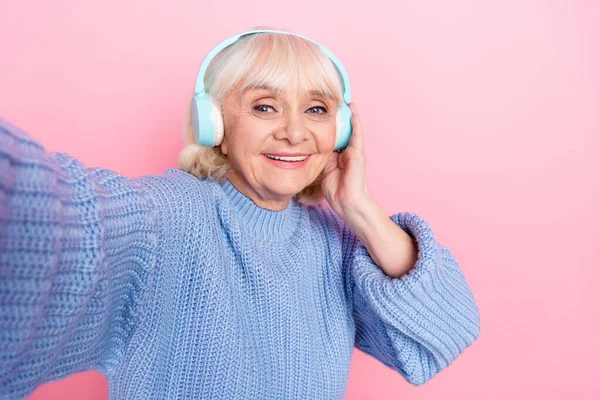 Автопортрет привлекательной веселой седой женщины, слушающей поп-сингл mp3 песни, выделенный на фоне розового пастельного цвета — стоковое фото