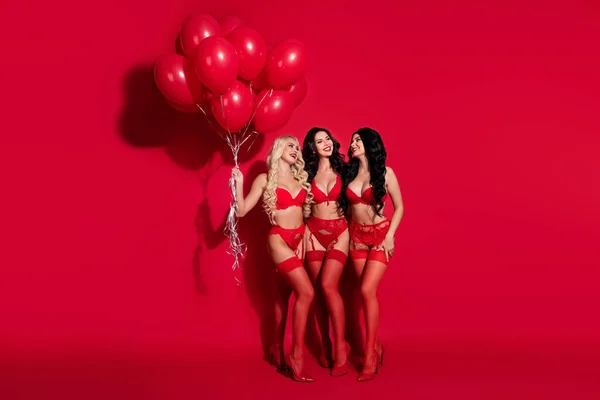 三个迷人而快乐的女孩抱着盛装的舞会，在明亮的红色背景下拥抱，全长身材 — 图库照片