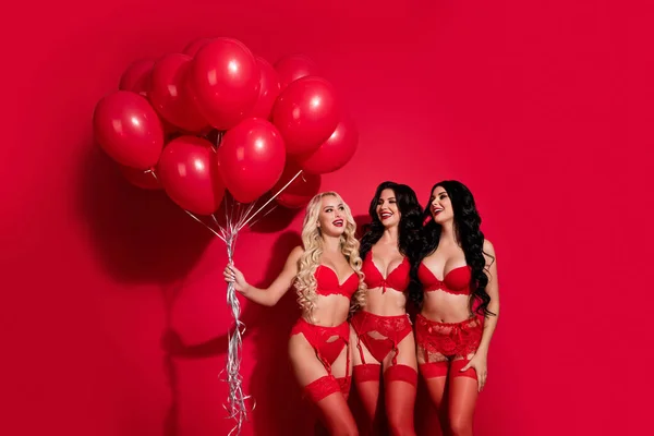 매력적 인 세 명의 명랑 한 소녀가 밝은 붉은색 배경에서 고립된 낭만적 인 성 관계를 가진 불알을 들고 있는 것을 판매하는 장면 — 스톡 사진