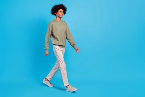 Full storlek profil sida foto av ung stilig man promenad ser tomt utrymme slitage casual outfit isolerad över blå färg bakgrund — Stockfoto