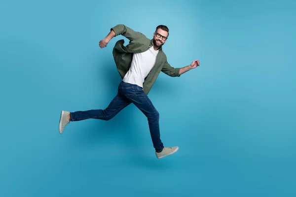 Profil zdjęcie wesoły miły facet skok sportowy bieg nosić specyfikacje zielony koszula dżinsy izolowane niebieski kolor tło — Zdjęcie stockowe