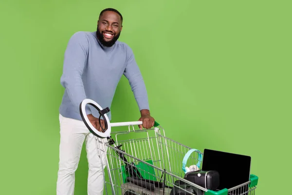 Fotografie veselý africký chlap oblečený svetr chůze nákupní zásobník gadgets izolované zelené barvy pozadí — Stock fotografie