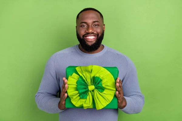Fotografie vzrušený africký chlap oblečený šedý svetr s úsměvem drží velký luk dárek izolované zelené barvy pozadí — Stock fotografie