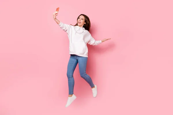 Foto de señora brillante excitada usar sudadera con capucha blanca sonriendo saltando alta grabación brazo de vídeo espacio vacío aislado color rosa fondo —  Fotos de Stock