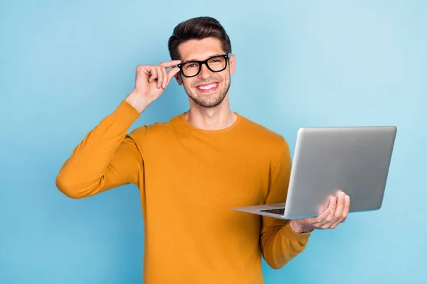 Foto de hombre joven bastante atractivo usar gafas de brazo suéter amarillo sonriendo sosteniendo gadget moderno aislado fondo de color azul — Foto de Stock