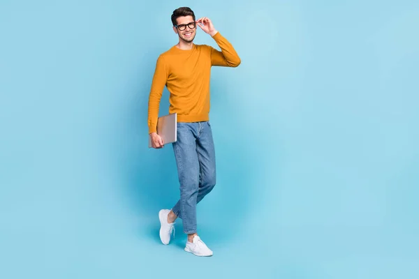 Fotografie atraktivní roztomilý mladý muž nosit žlutý svetr rameno brýle s úsměvem chůze držení moderní gadget izolované modré barvy pozadí — Stock fotografie