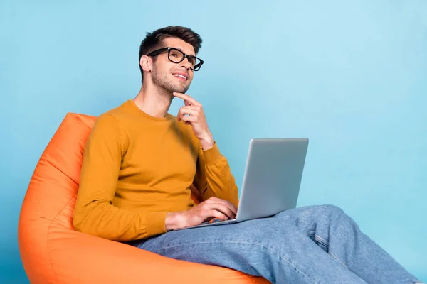 Portrett av en attraktiv, drømmende fyr som sitter i stolen og bruker laptop-maskin isolert over lys blå farge-bakgrunn – stockfoto