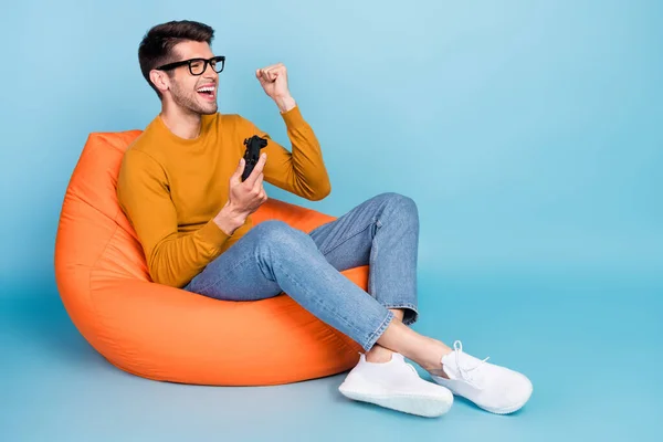 Retrato de cara alegre atraente sentado na cadeira jogando jogo se divertindo regozijando isolado sobre fundo de cor azul brilhante — Fotografia de Stock