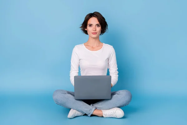 Foto de mujer bastante brillante usar camisa blanca piernas cruzadas mecanografía moderno gadget aislado color azul fondo — Foto de Stock