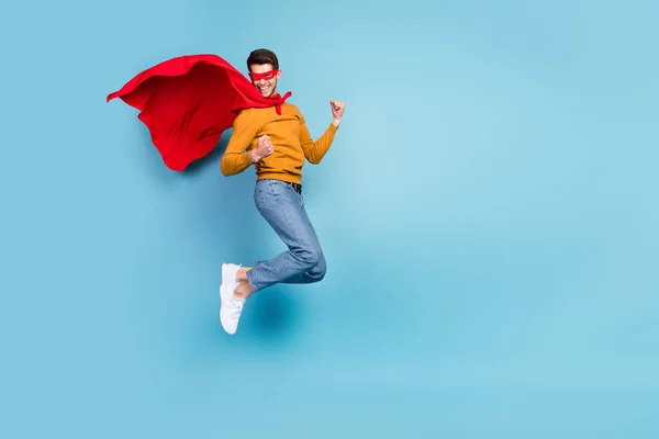Fénykép bájos szerencsés srác öltözött pulóver Superman jelmez ugrás emelkedő öklök üres tér mosolygós elszigetelt kék szín háttér — Stock Fotó