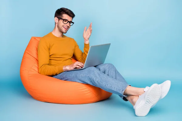 Portrét atraktivní veselý chlap sedí v křesle pomocí notebooku volání kontakt izolované přes jasně modrou barvu pozadí — Stock fotografie