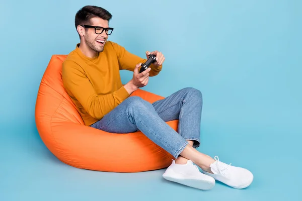 Retrato de chico alegre atractivo sentado en silla jugando videojuego divertirse tiempo libre aislado sobre fondo de color azul brillante —  Fotos de Stock