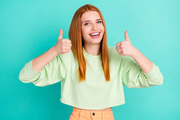 Фото позитивної красивої молодої жінки в зеленому вбранні, що показує два великі пальці вгору посміхаючись ізольований бірюзовий кольоровий фон — стокове фото