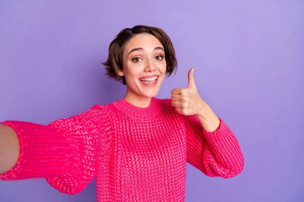 밝고 예쁜 소녀가 셀카를 하는 사진은 엄지손가락 이 보라색 배경에 고립된 뜨개 질 스웨터를 입고 있음을 보여준다 — 스톡 사진