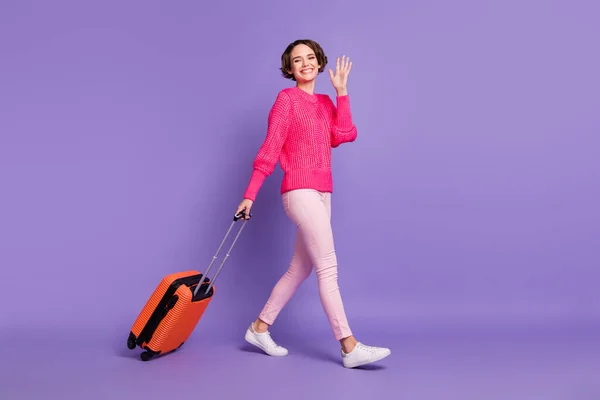 Полный профиль тела портрет положительной красивой девушки ходьба нести чемодан ладонь волна изолированы на фиолетовом фоне цвета — стоковое фото