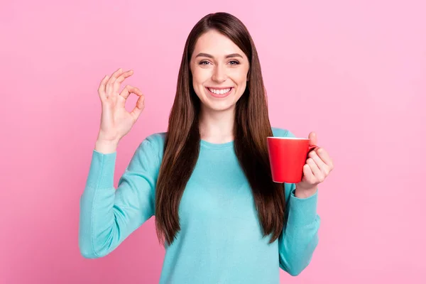 Photo portrait of girl keeping coffee mug showing okay gesture isolated on pastel pink color background — Stock Photo, Image