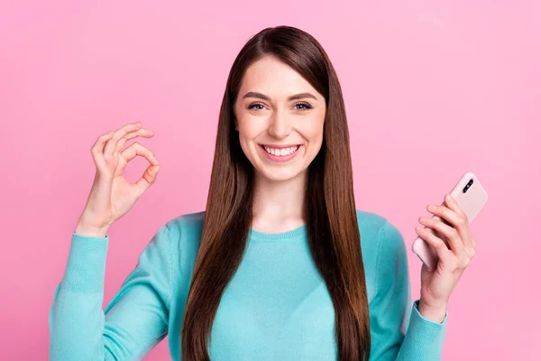 Portrét atraktivní veselá dívka drží v ruce zařízení ukazující ok-sign reklama izolované přes růžové pastelové barvy pozadí — Stock fotografie
