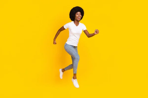 Foto de longitud completa de la señora de piel oscura bastante dulce usar camiseta blanca saltando alto corriendo rápido sonriendo aislado color amarillo fondo —  Fotos de Stock