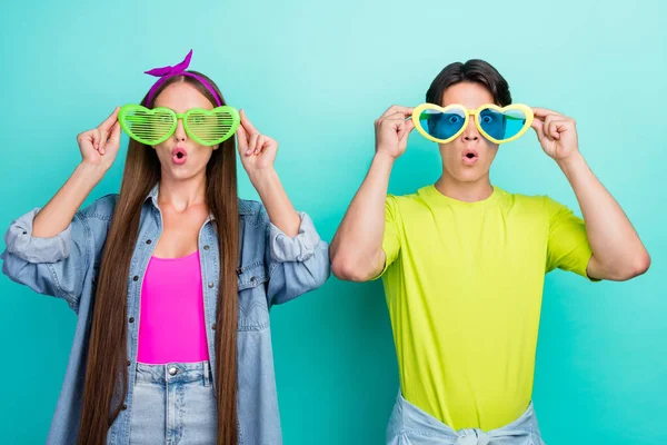 Foto de brincalhão morena jovem casal tentar eyewear desgaste colorido camisetas isoladas no fundo cor teal — Fotografia de Stock