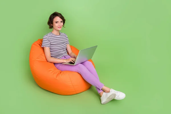 Foto wanita lucu mengkilap berpakaian bergaris t-shirt duduk kantong kacang mengetik perangkat modern ruang kosong mengisolasi latar belakang warna hijau — Stok Foto