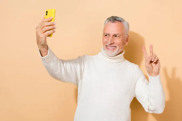 Çekici, gri saçlı, selfie çeken, bej renkli pastel arka planda izole edilmiş v-işareti blogları gösteren bir adamın portresi. — Stok fotoğraf