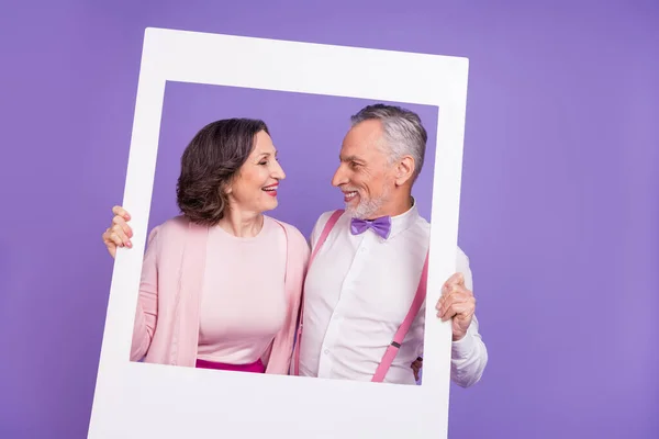 Фото идиллических двух партнеров держат бумажную карточку альбома смотреть друг на друга изолированы на фиолетовом фоне — стоковое фото