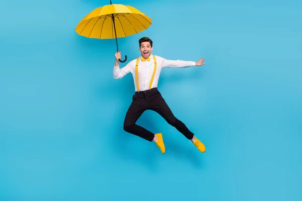 Retrato de comprimento total de cara bonito enérgico segurar guarda-chuva voando isolado no fundo de cor azul — Fotografia de Stock