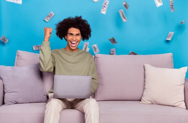 Foto anak muda bersukacita kepalan tangan kemenangan menggunakan laptop terbang uang keuntungan yang terisolasi dari latar belakang warna biru — Stok Foto