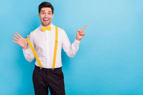 Foto van opgewonden mooie man dragen gele bretels wit shirt wijzend vinger lege ruimte geïsoleerde blauwe kleur achtergrond — Stockfoto