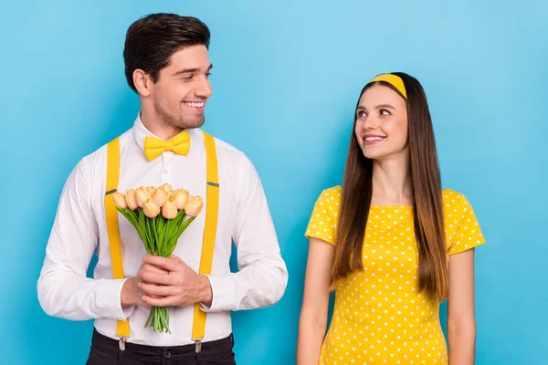 Foto van twee vreedzame idyllische partners kijken elkaar houden gele tulpen geïsoleerd op blauwe kleur achtergrond — Stockfoto