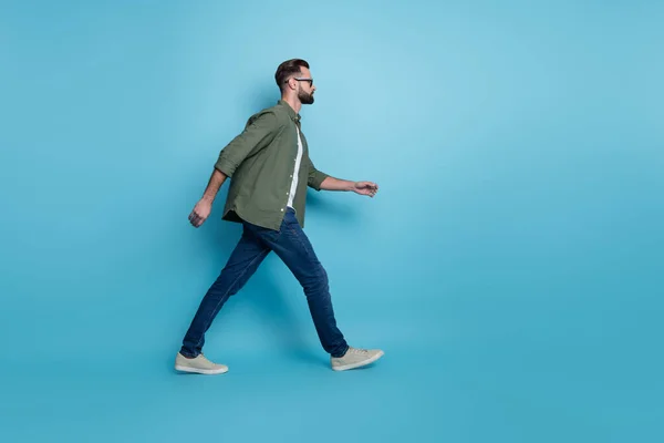 Foto de perfil de un empleado inteligente caminar pasos de carrera llevar gafas camisa verde jeans aislado color azul fondo — Foto de Stock