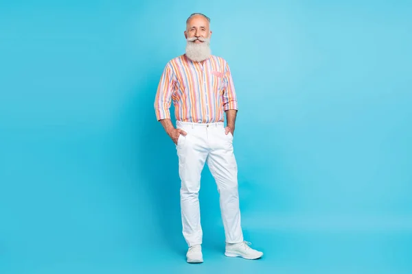 Photo of cheerful grandfather palms pockets toothy smile wear striped shirt pants sneakers isolated blue color background — Stock Photo, Image