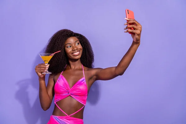 Foto sladké veselá africká dáma oblečené růžové sexy oblečení pití révy nahrávání videa moderní zařízení izolované fialové barvy pozadí — Stock fotografie