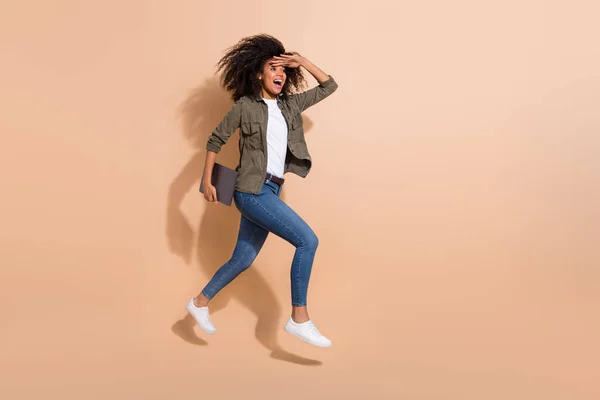 フル長いですボディサイズビューのかなり陽気な女の子ジャンプ運ぶラップトップ発見方法隔離された上ベージュパステルカラーの背景 — ストック写真