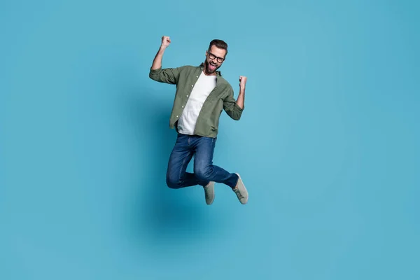 Фото веселый удивленный парень прыгать радоваться триумф носить очки зеленая рубашка изолированный синий цвет фона — стоковое фото