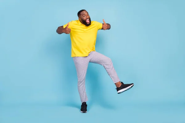 Foto van grappige zoete donkere huid man dragen gele t-shirt dansen tonen duimen glimlachen geïsoleerde blauwe kleur achtergrond — Stockfoto