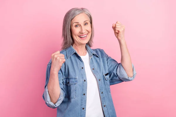 Foto de senhora madura muito sortuda usar roupas jeans levantando punhos sorrindo isolado cor de fundo rosa — Fotografia de Stock
