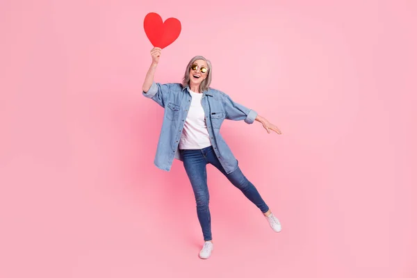 Corpo inteiro foto de feliz encantador alegre mulher velha pegar mão grande vermelho papel coração isolado no fundo cor-de-rosa — Fotografia de Stock