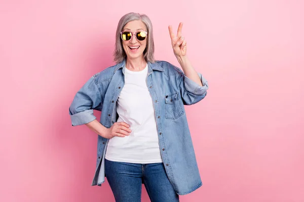 Φωτογραφία του χαιρετισμού ηλικιωμένη κυρία δείχνουν v-σημάδι φορούν γυαλιά μπλε σακάκι λευκό t-shirt που απομονώνονται σε ροζ φόντο χρώμα — Φωτογραφία Αρχείου