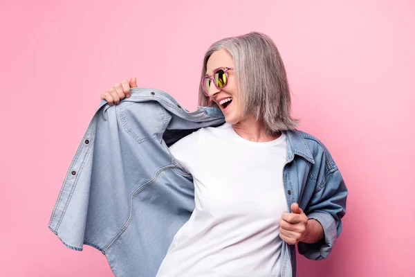 Foto de brillante adorable mujer de edad vestido jeans traje sonriente baile aislado color rosa fondo — Foto de Stock