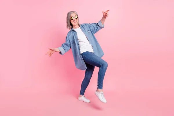 Foto de cuerpo completo de señora anciana loca danza desgaste blazer azul jeans zapatillas aisladas sobre fondo de color rosa — Foto de Stock