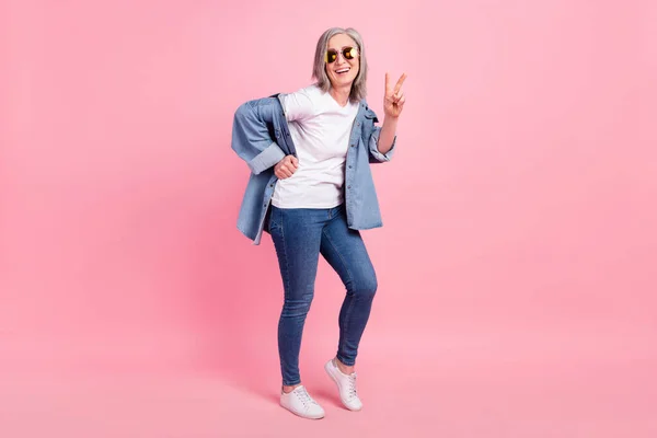 Foto de tamaño completo de saludo señora madura espectáculo v-signo desgaste gafas camisa jeans aislados sobre fondo rosa — Foto de Stock
