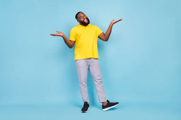 Photo of sweet excited dark skin guy dressed yellow t-shirt shrugging shoulders smiling isolated blue color background — Stock fotografie