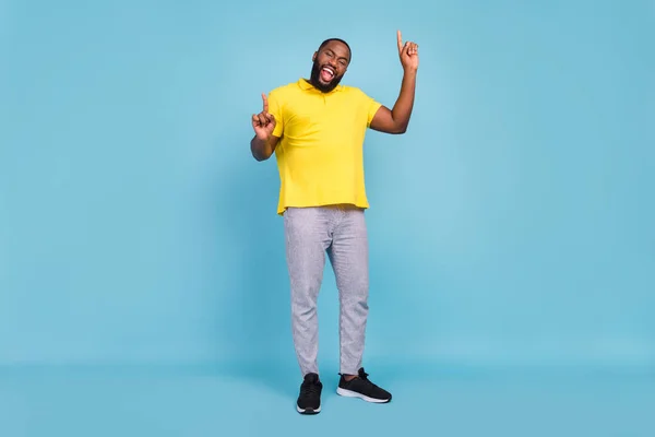 Foto de chico de piel oscura bastante dulce vestido camiseta amarilla sonriendo señalando los dedos espacio vacío aislado color azul fondo —  Fotos de Stock